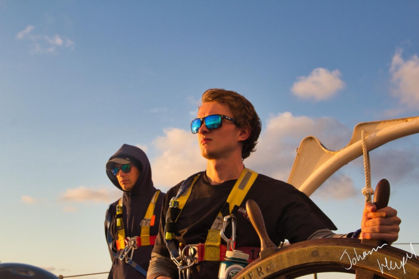 Picture shows a student at the helm of a sailing ship near sundown