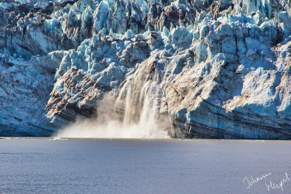 Picture shows snow pouring off the side of a craggy glacier into the ocean